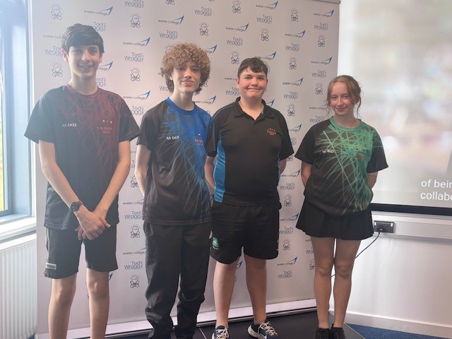 Four students in PE kits stood smiling on a small stage