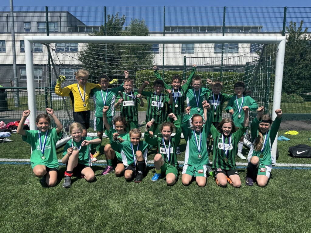 Pupils sat in a row on the football pitch, with a row of pupils stood behind celebrating their win and wearing their green football kit