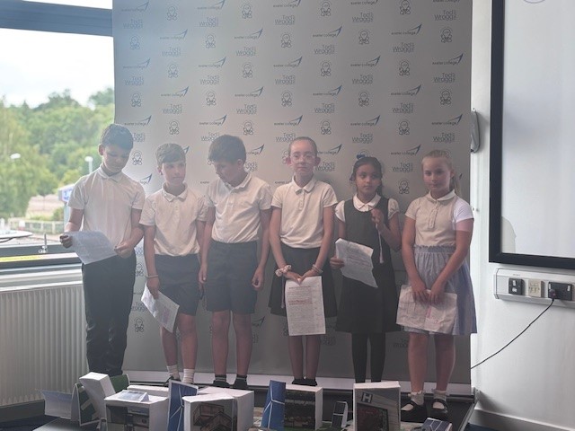 Six young students in uniform stood on a small stage with presentation notes in hand