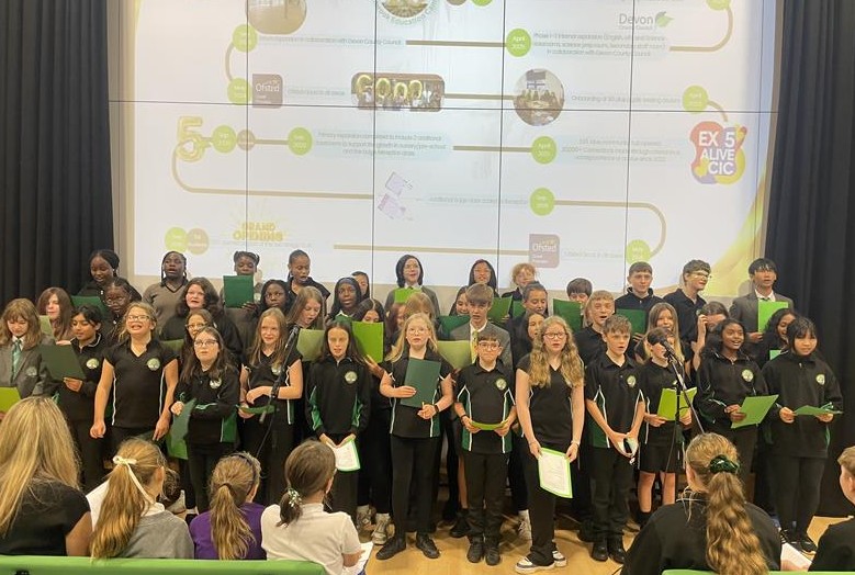 Students stood in rows at front of hall singing in choir