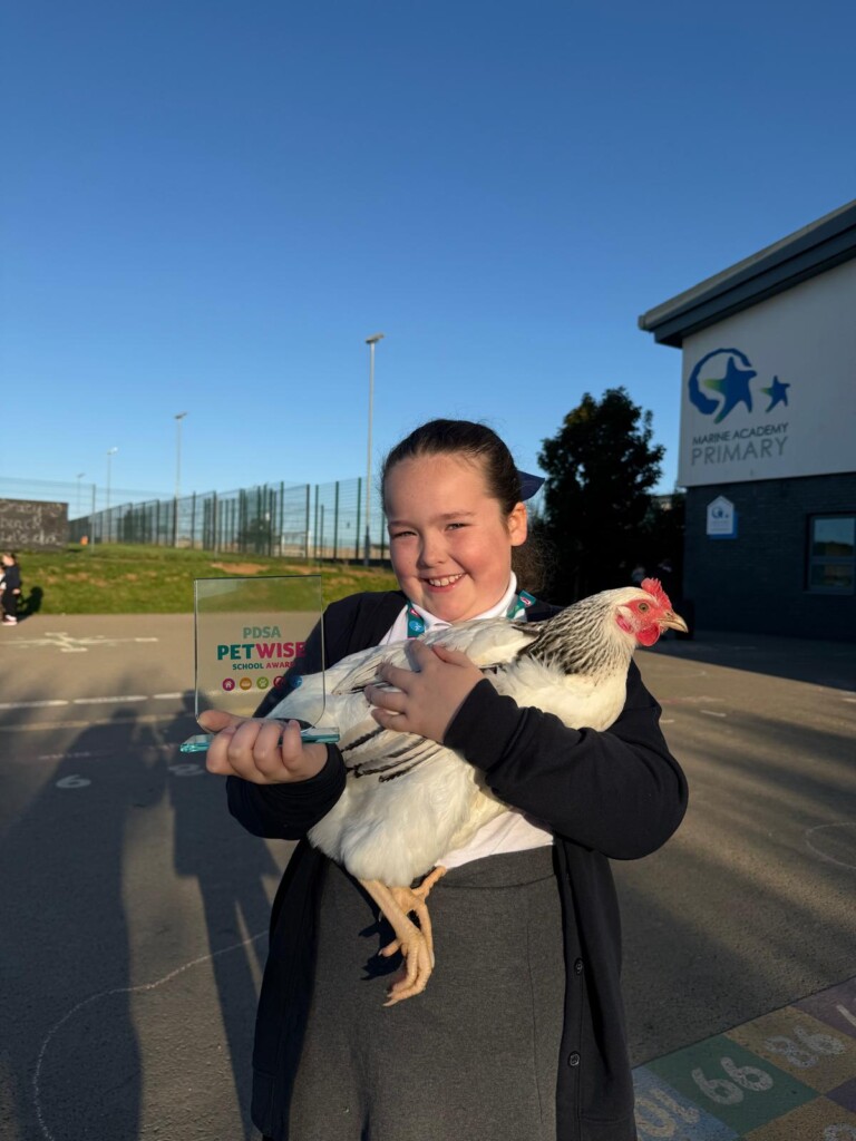 Student stood in playground holding a chicken in one arm and an trophy in another