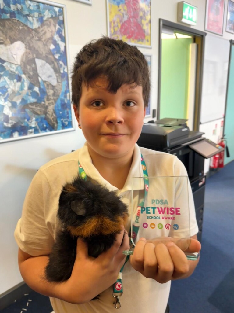 Student stood in a classroom holding a brown guinea pig in one hand and an award trophy in another