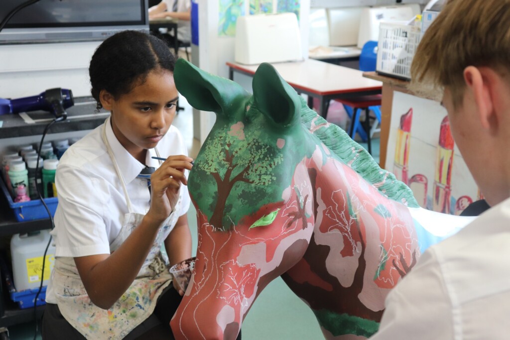 Student painting a model horse in green and pink