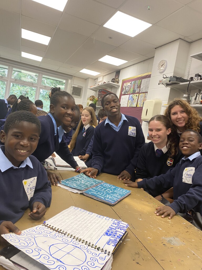Group of students sat at a wooden desk crowded round looking at art books