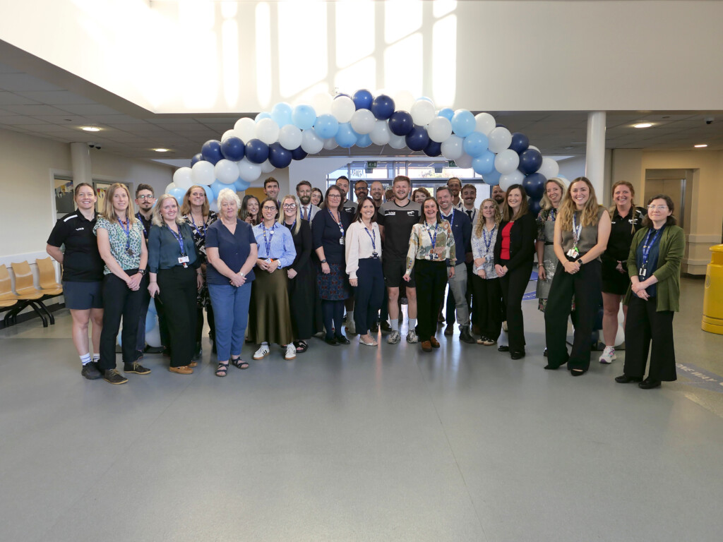 Staff stood in a school canteen in front of a blue balloon arch