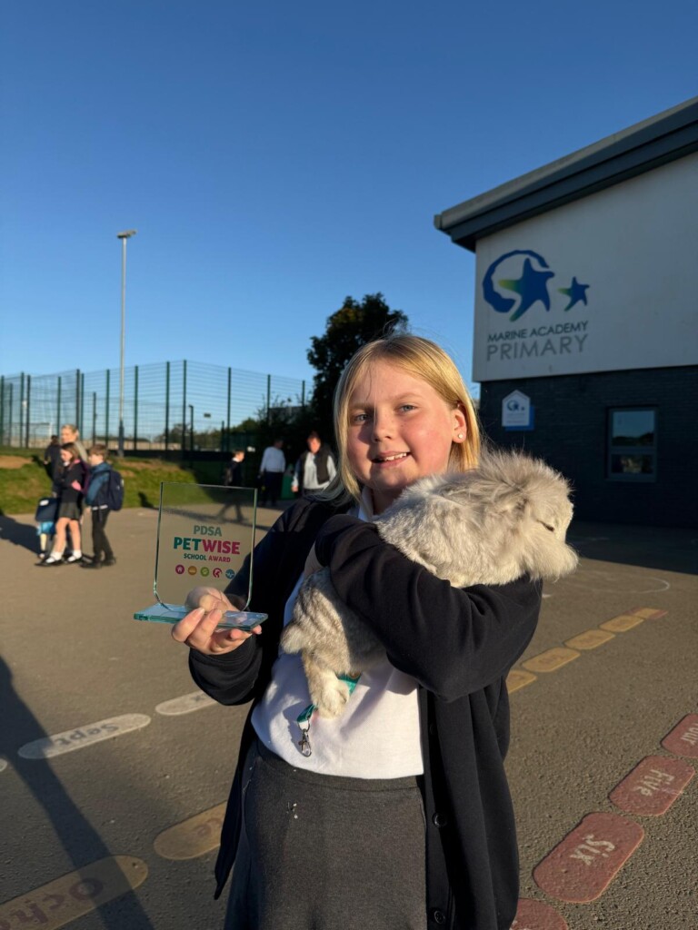 Student stood in playground holding a bunny rabbit in one arm and a trophy in another