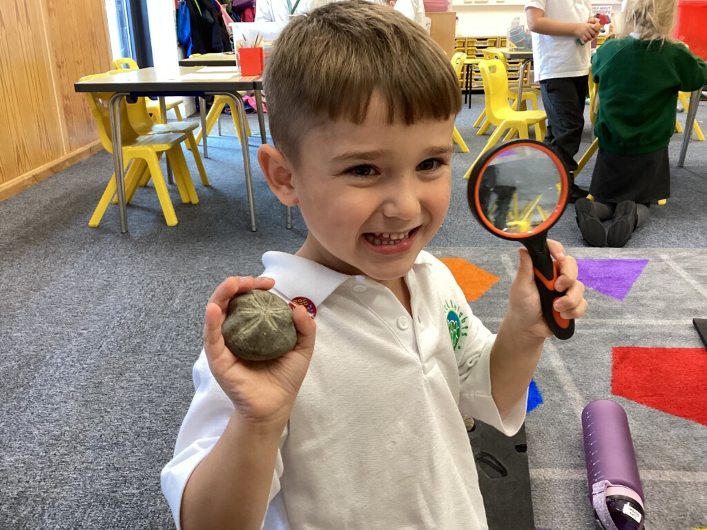 Student sat smiling at the camera holding a magnifying glass