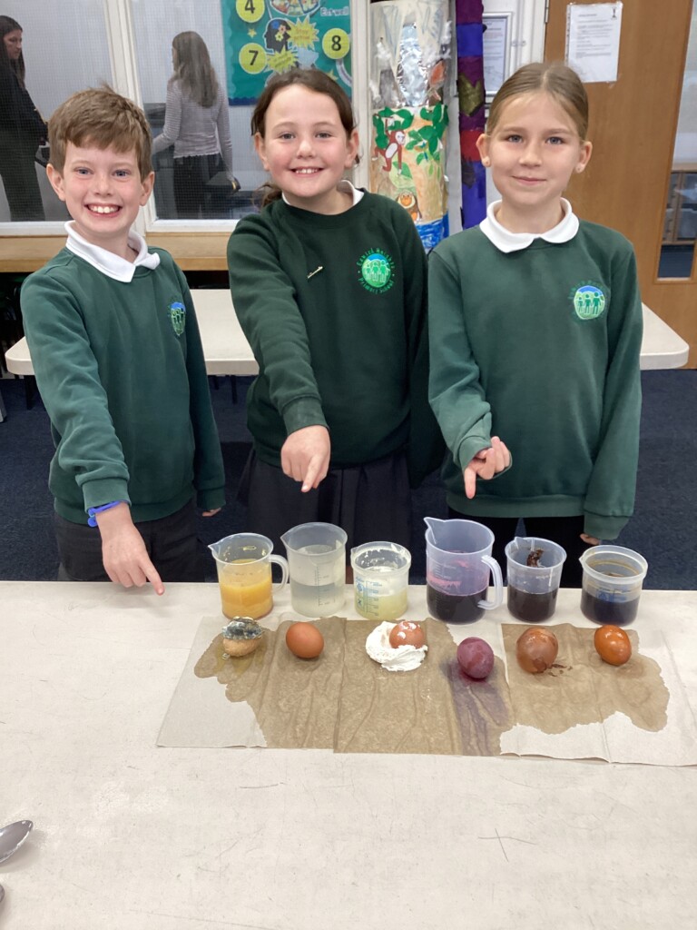 Three students in uniform stood pointing at a science experiment