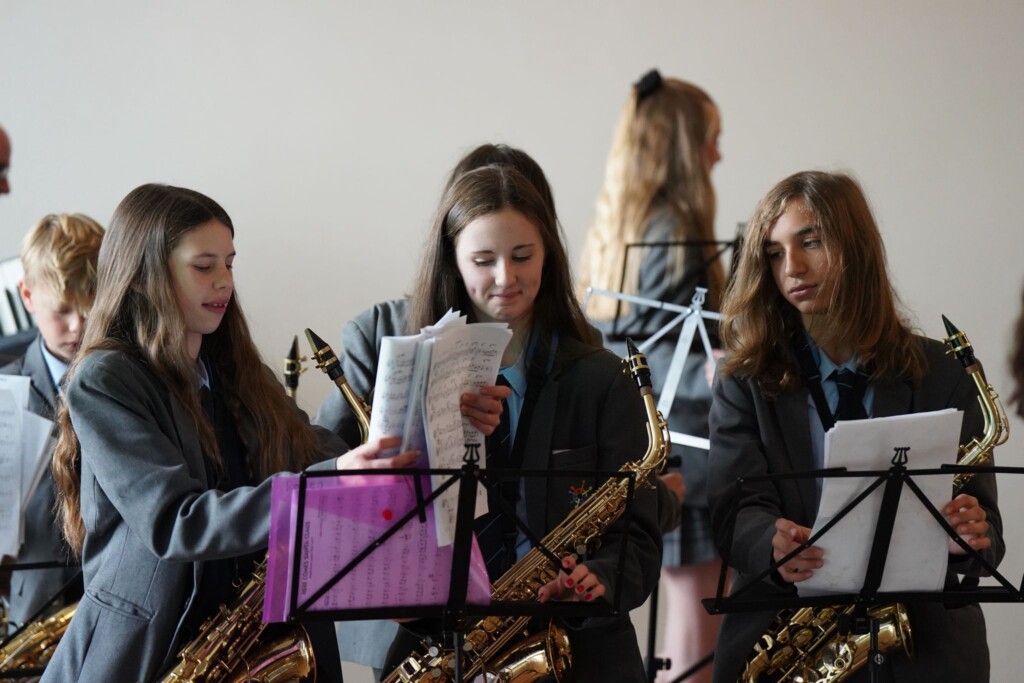 Three students with saxophones and turning their sheet music