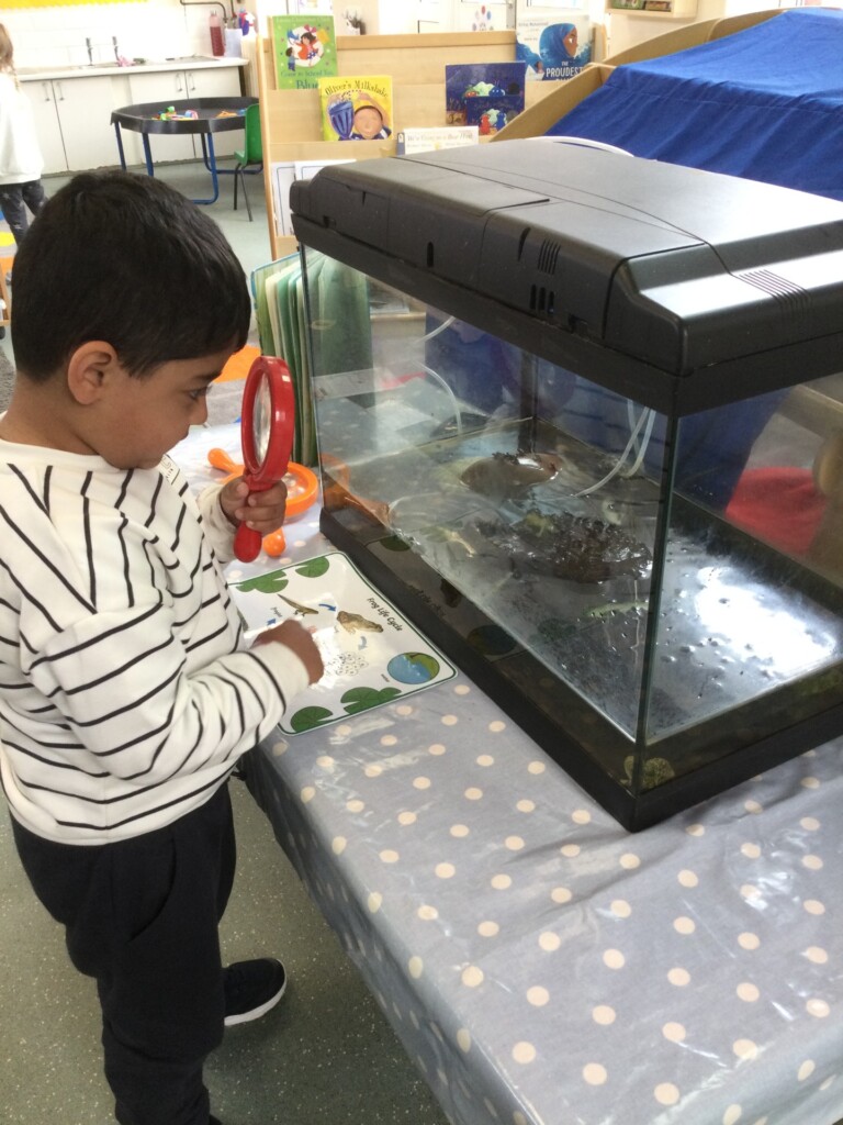 Child in stripey top stood using magnifying glass
