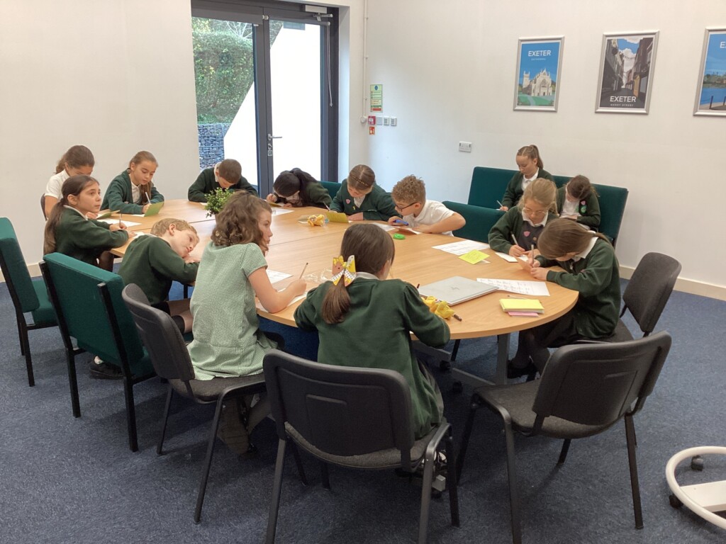 Several children in school uniform sat at a brown table writing cards