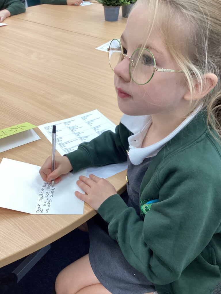Child in school uniform sat at a brown table writing on a white card