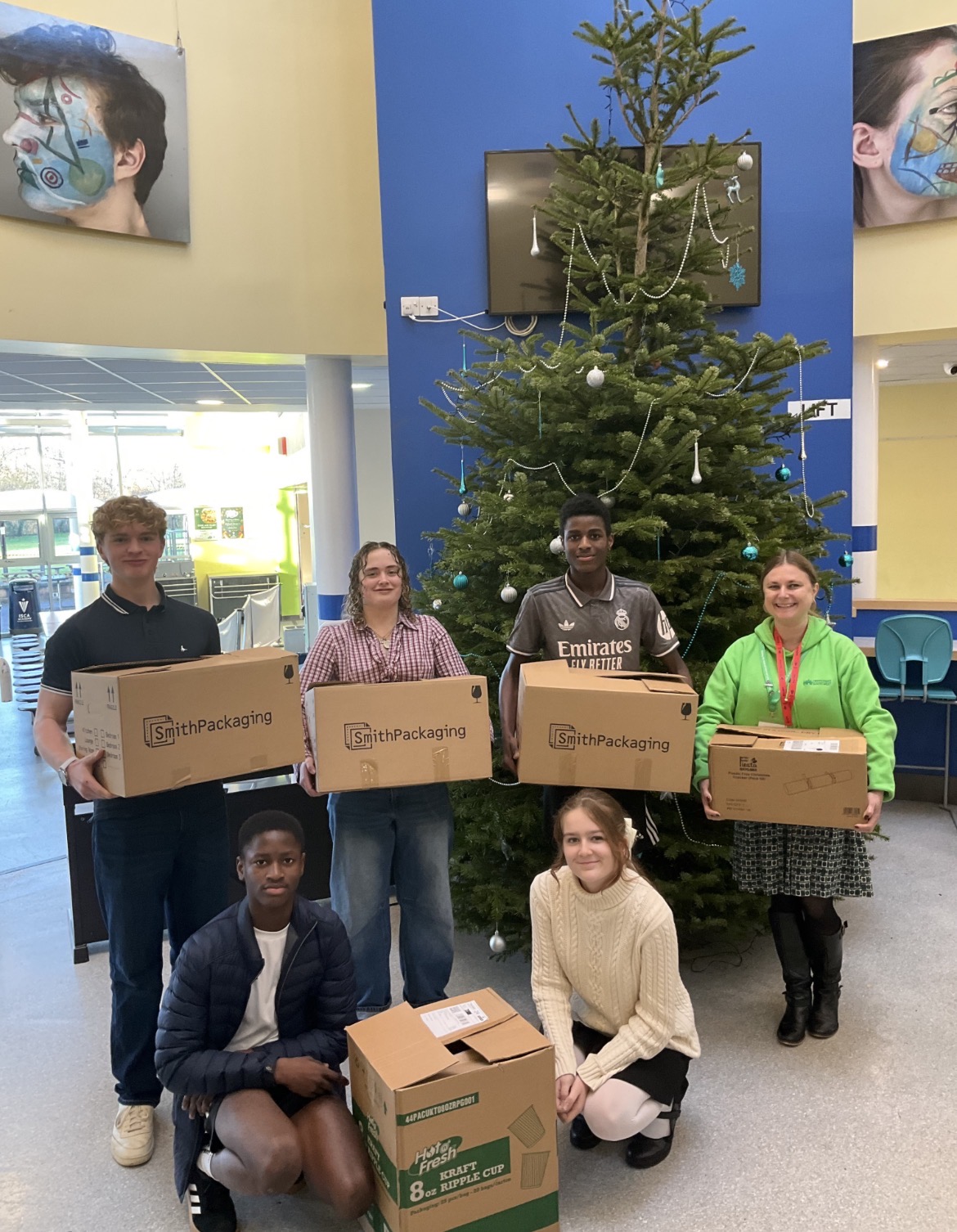 A group of students stood in front of a Christmas tree holding boxes of books