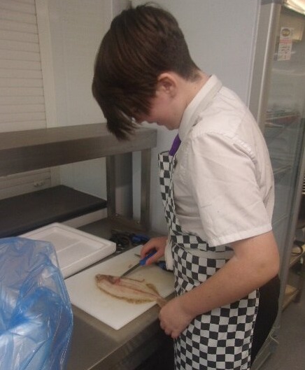 All Saints Student chopping fish in the kitchen