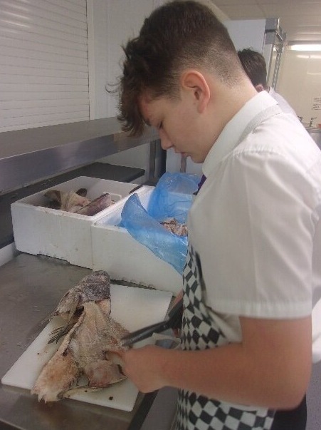 All Saints Student chopping fish in the kitchen