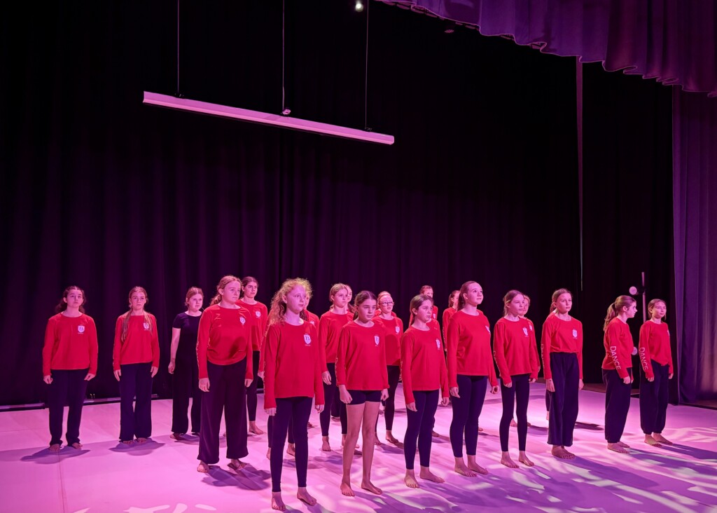 student dancers on stage all dressed in red tops and black trousers stood in trop formation