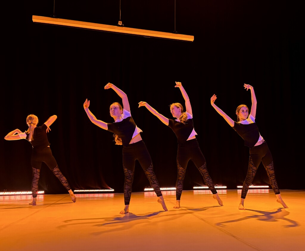 student dancers on stage with hands in the air bending to the side.