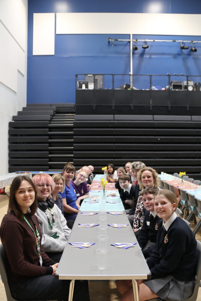 Exmouth Community sat at tables sharing food and talking with daffodils on the table 