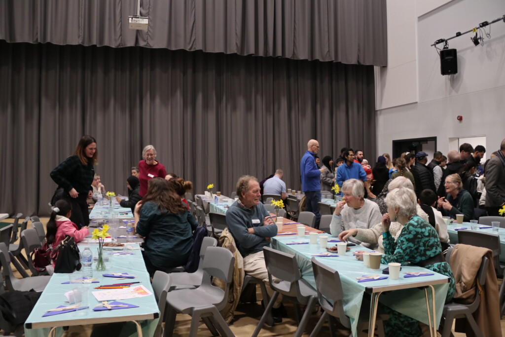 Exmouth Community sat at tables sharing food and talking with daffodils on the table 