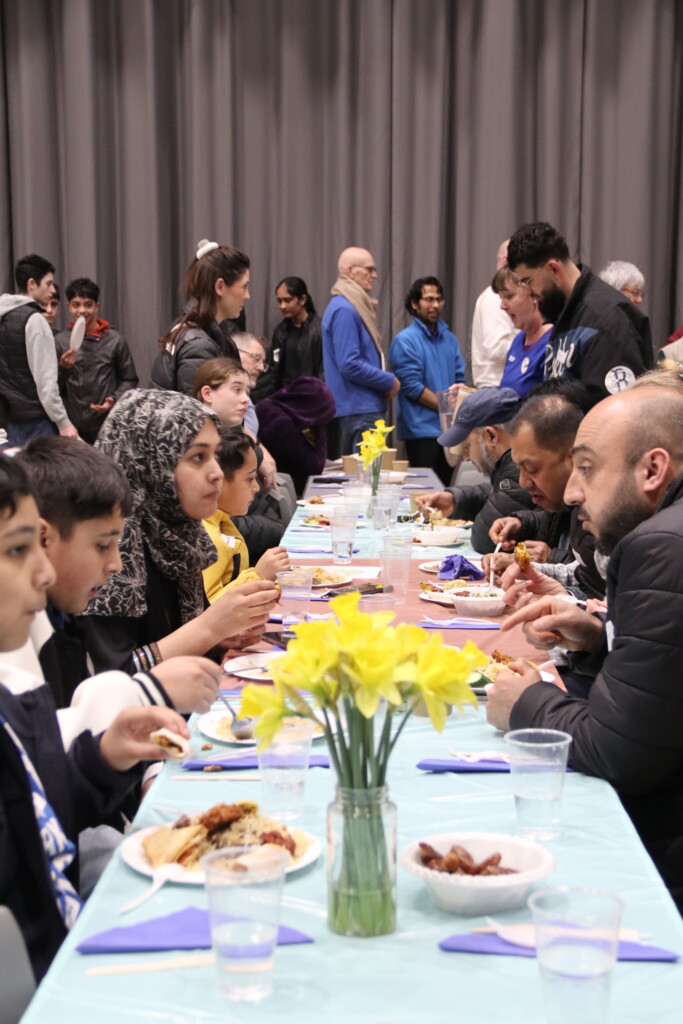 Exmouth Community sat at tables sharing food and talking with daffodils on the table 