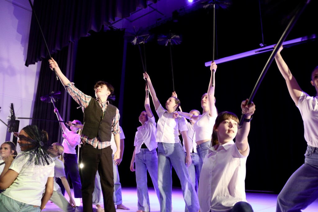 student dancers on stage with hands in the air bending to the side.