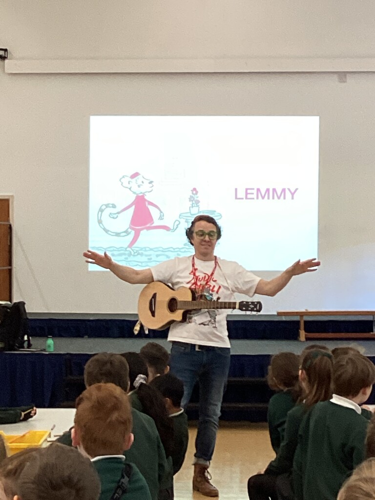 Alex Milway with his guitar standing infront of a presentation slide