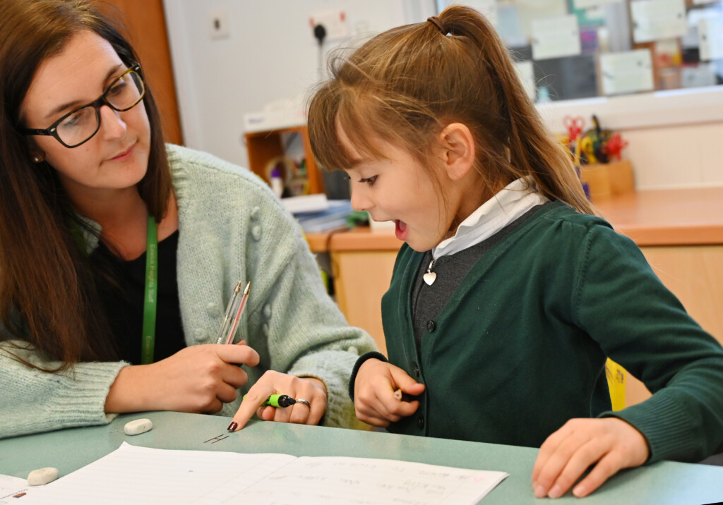 Student sitting at table being taught by a teacher