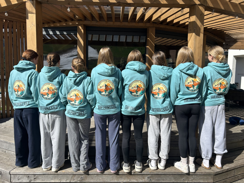 A group of students facing backwards to show the branded hoodies they are wearing.