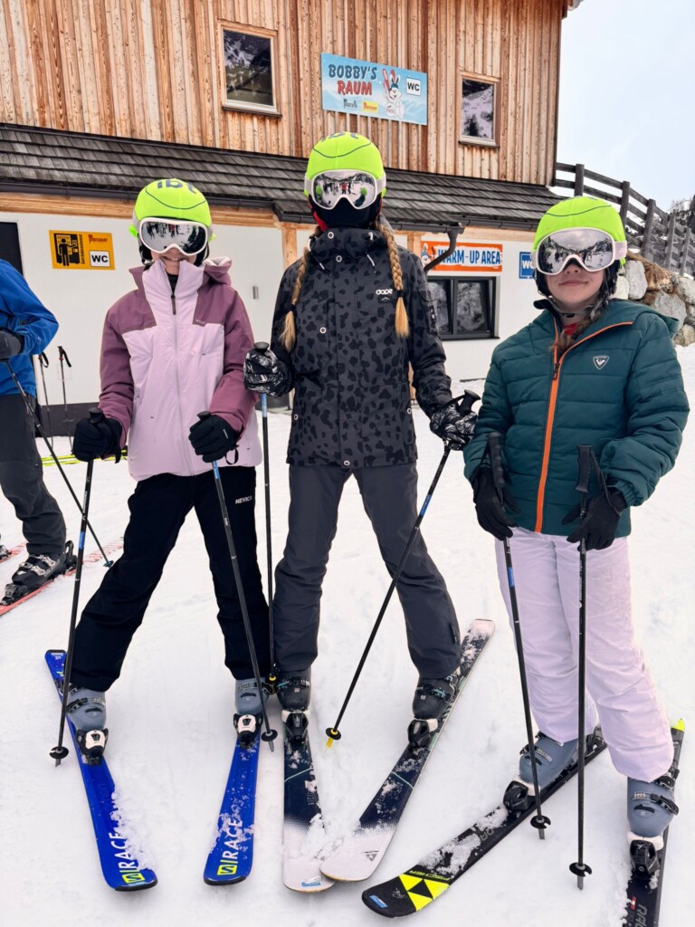 3 students on skis smiling at the camera.