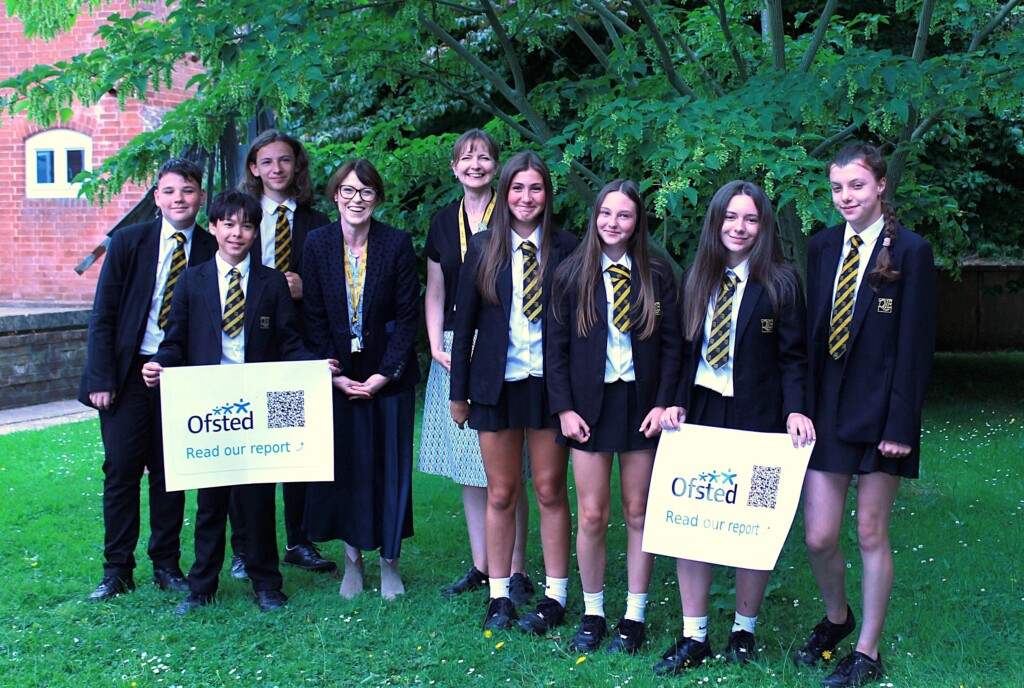 Group of students and staff smiling holding Ofsted posters