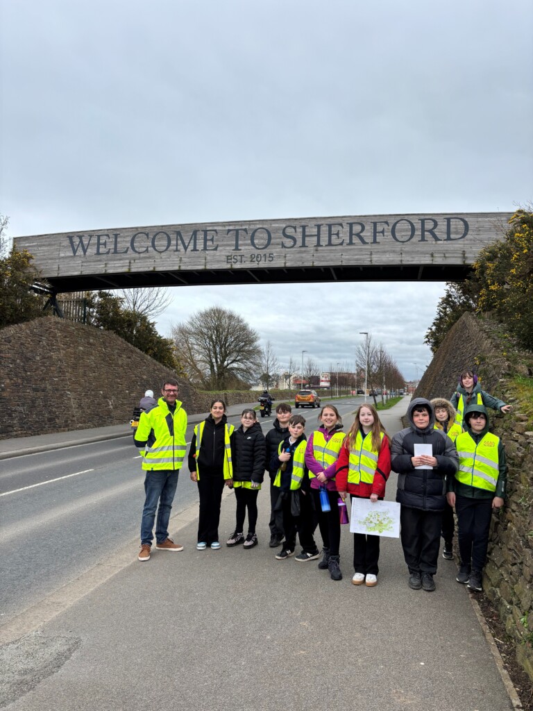 Group of students stood underneath the 'Welcome to Sherford' sign.