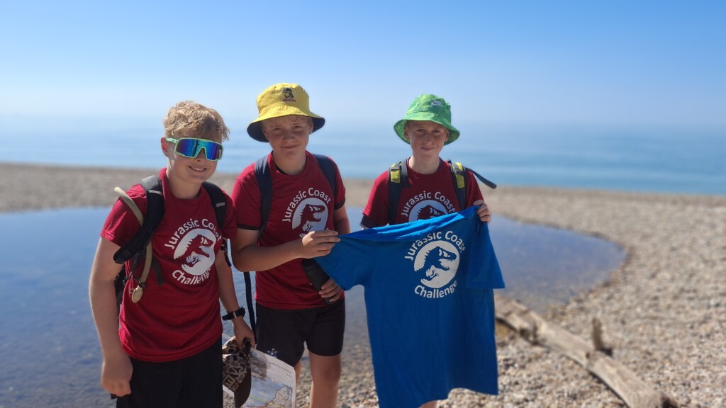 3 students celebrating finishing the challenge, holding a blue t shirt