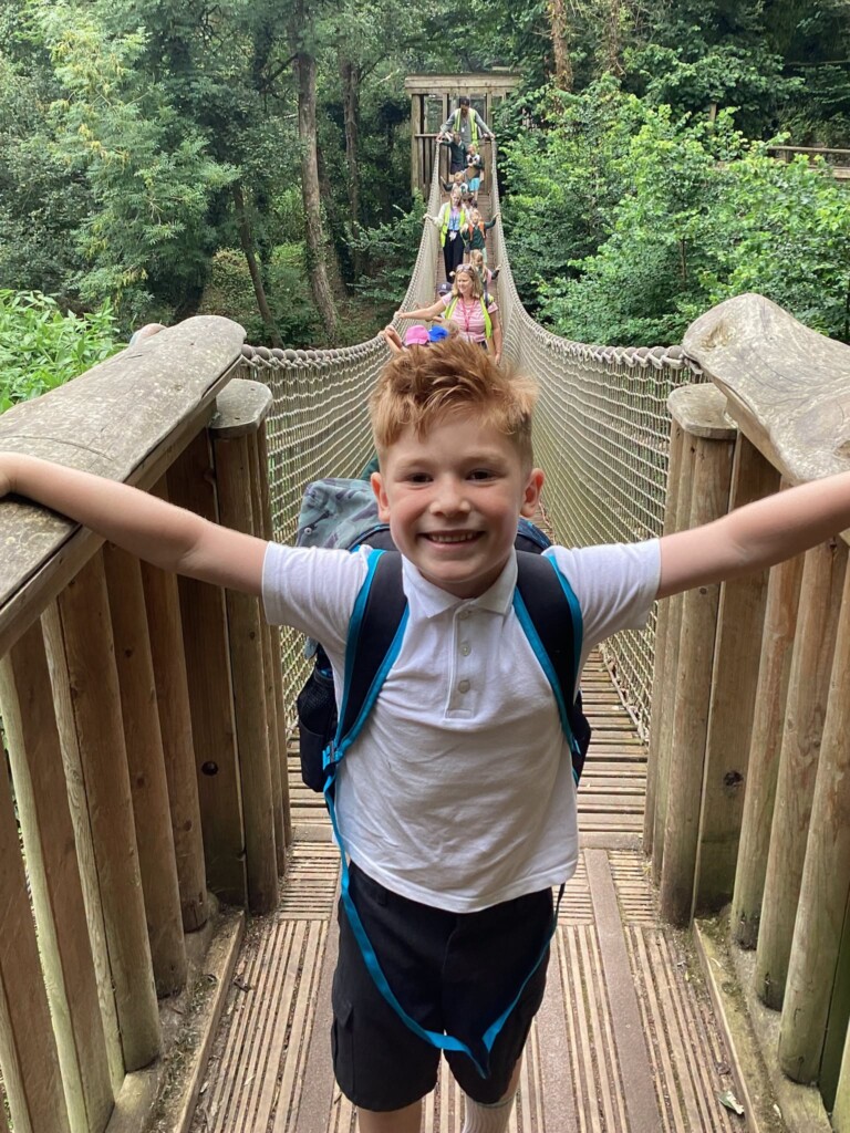 A pupil smiling as he reaches the end of a long bridge through the trees