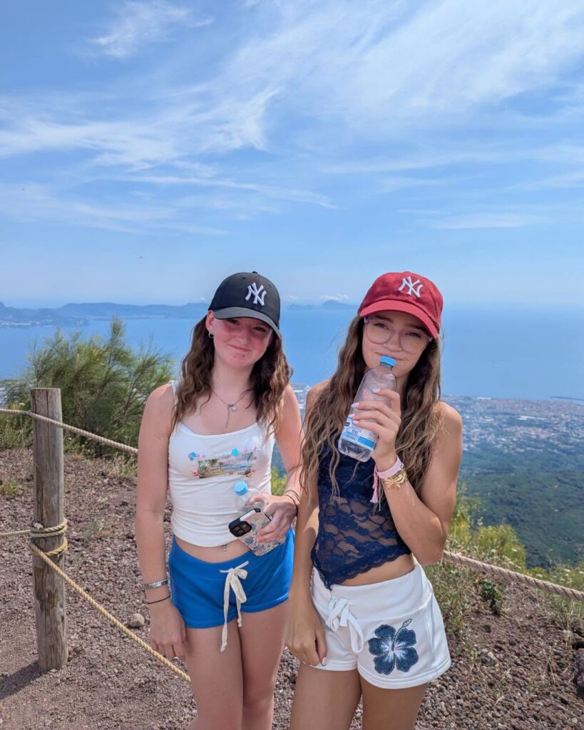 Two students smiling at the camera with a view of the sea and landscape behind them
