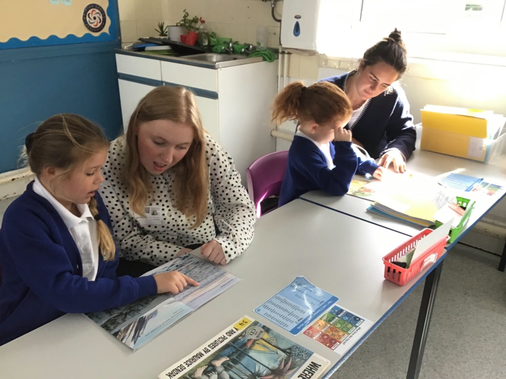 Two trainee teachers sat with a pupil each, reading together.
