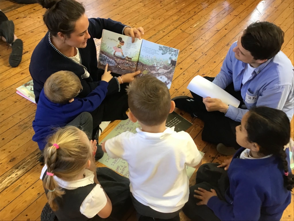 A trainee teacher holding a book and reading out loud to a group of pupils