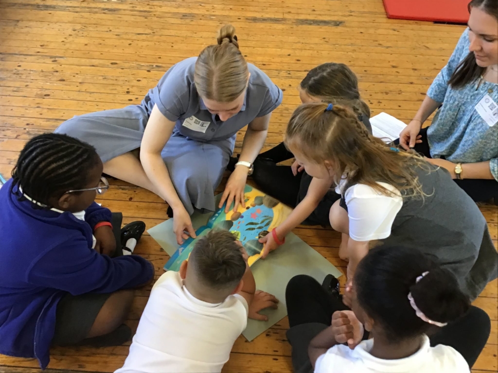 Two trainee teachers with 4 pupils, looking at a children's book.